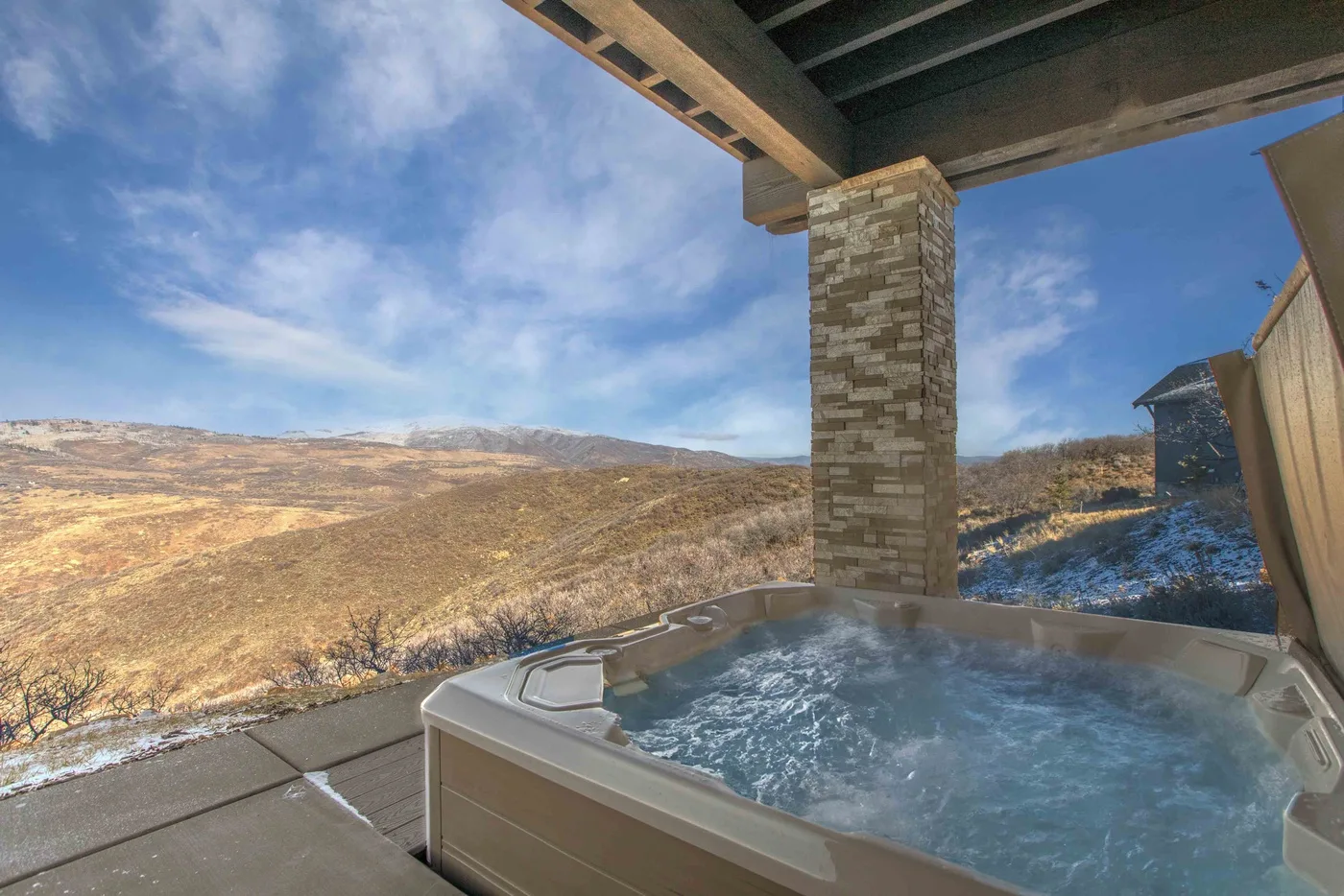An outdoor hot tub sits on a covered terrace overlooking a snow-dusted hillside.
