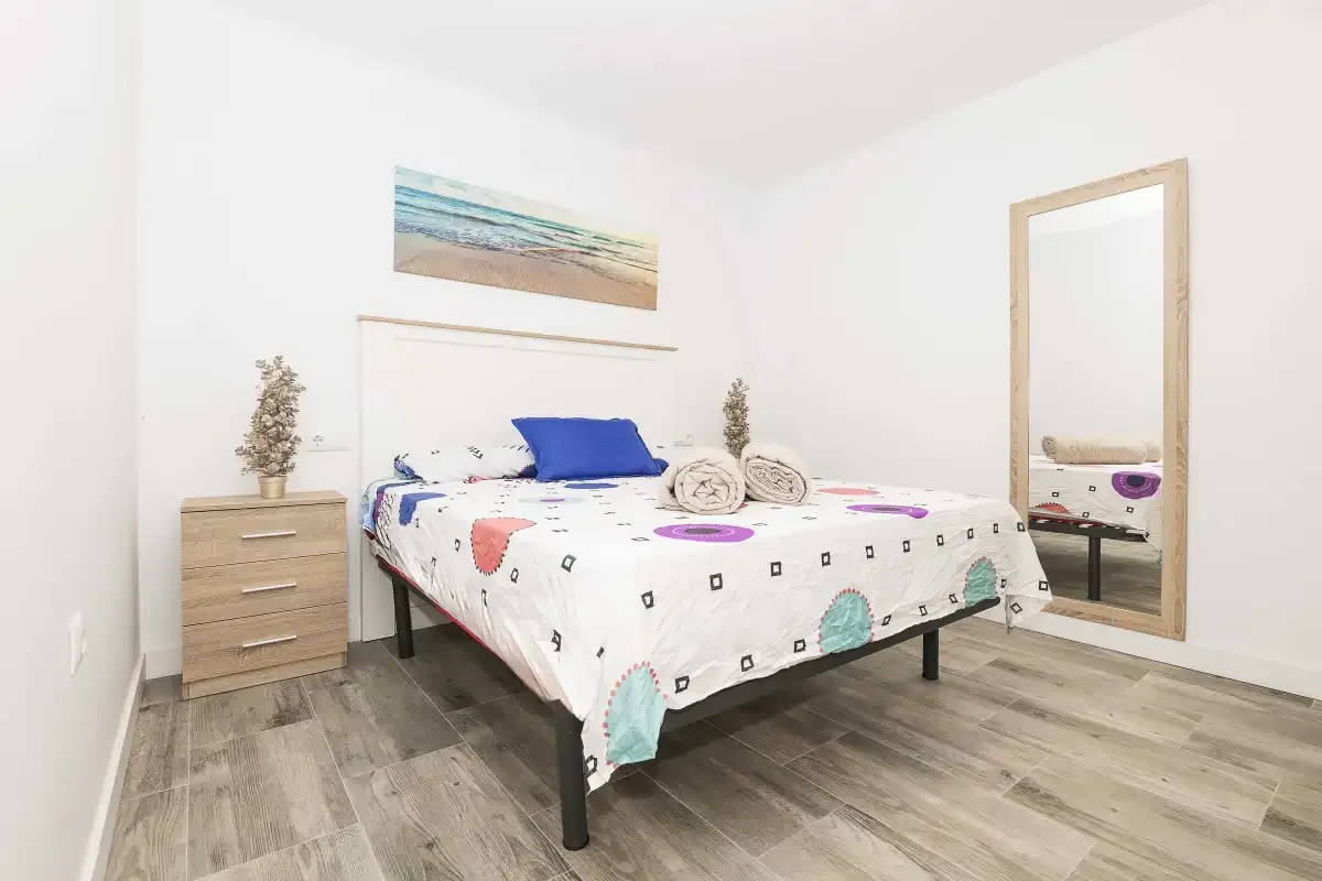 Un dormitorio luminoso con una cama doble y una imagen enmarcada de playa encima.