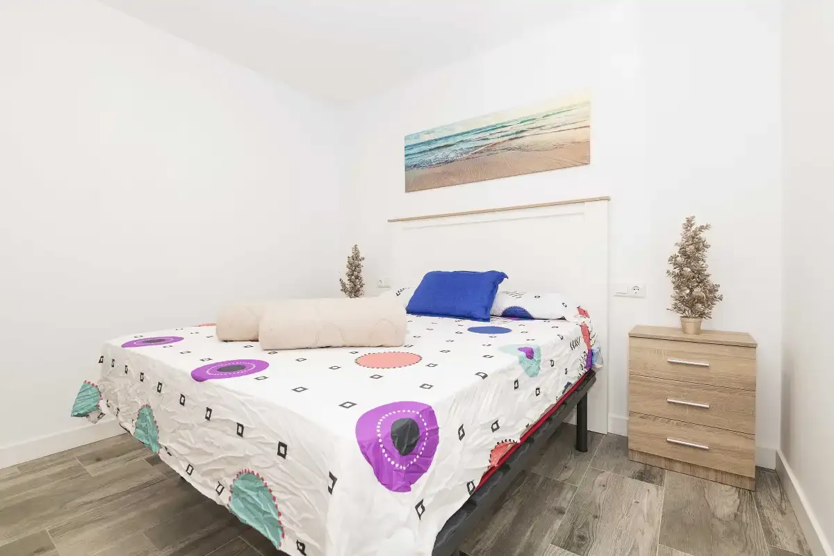 Un dormitorio con una colcha estampada y una mesita de madera.