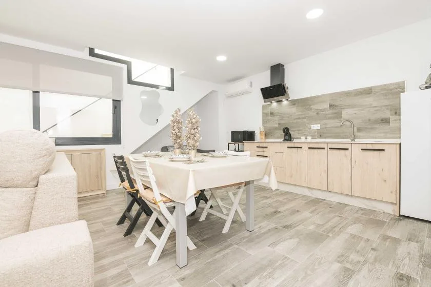 Una luminosa zona de comedor y cocina tiene una mesa junto a una encimera larga.