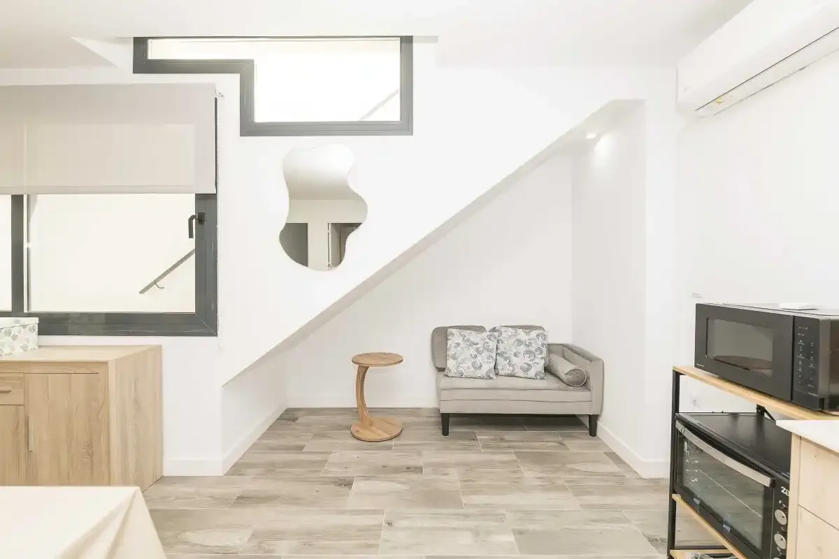 Una sala luminosa con un pequeño sofá bajo una escalera.