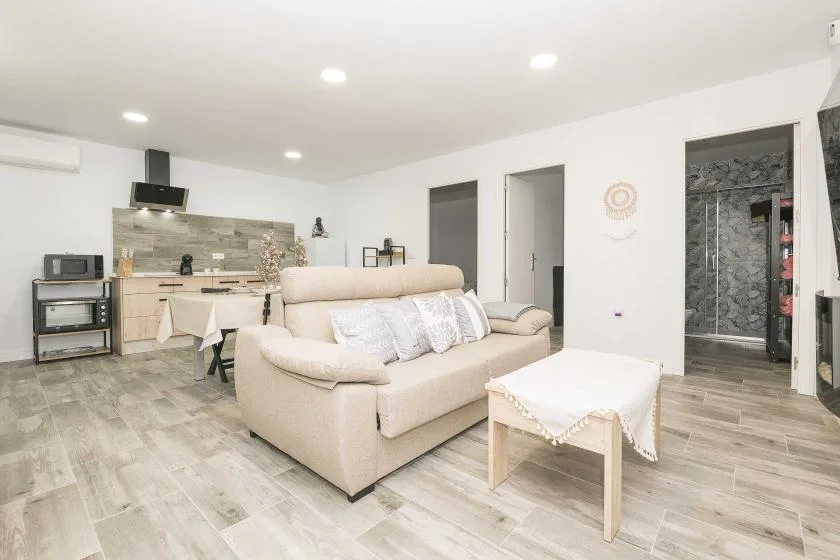 Una luminosa sala de estar con sofá beige, mesa de centro y cocina pequeña.