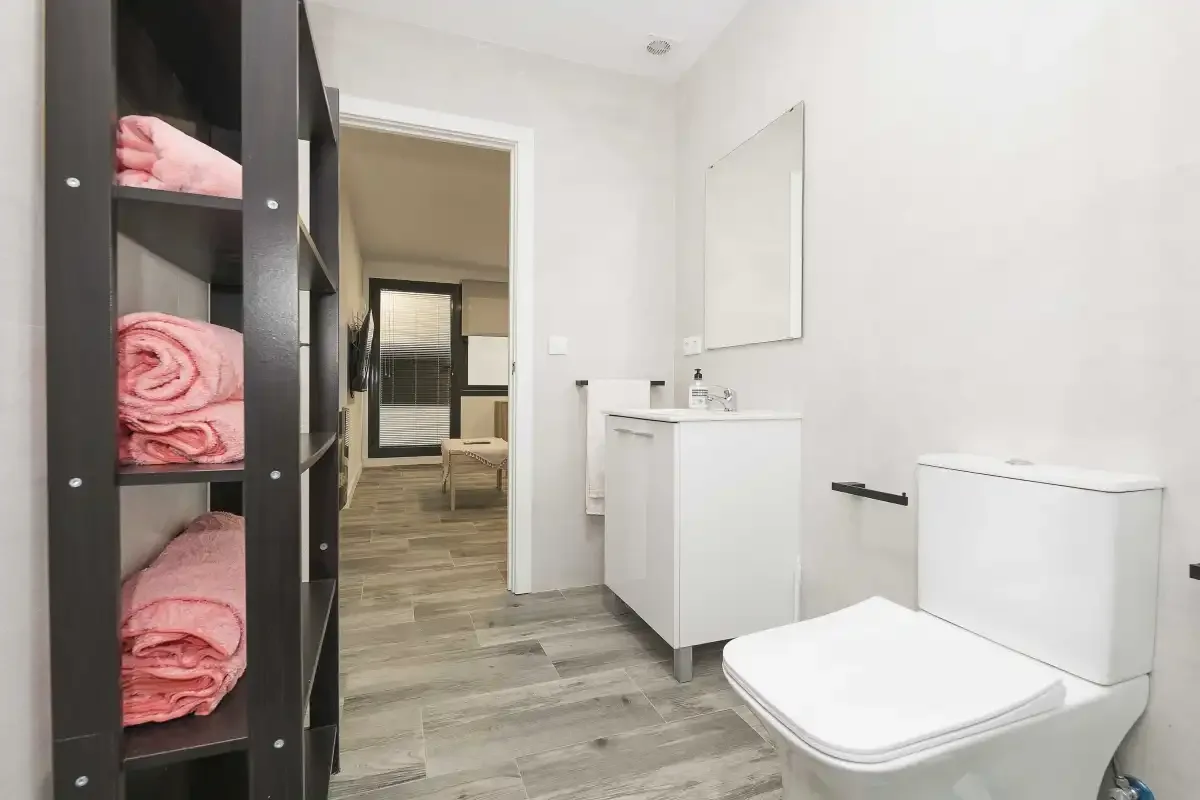 Un baño con lavabo, inodoro y toallas dobladas en estantes abiertos.