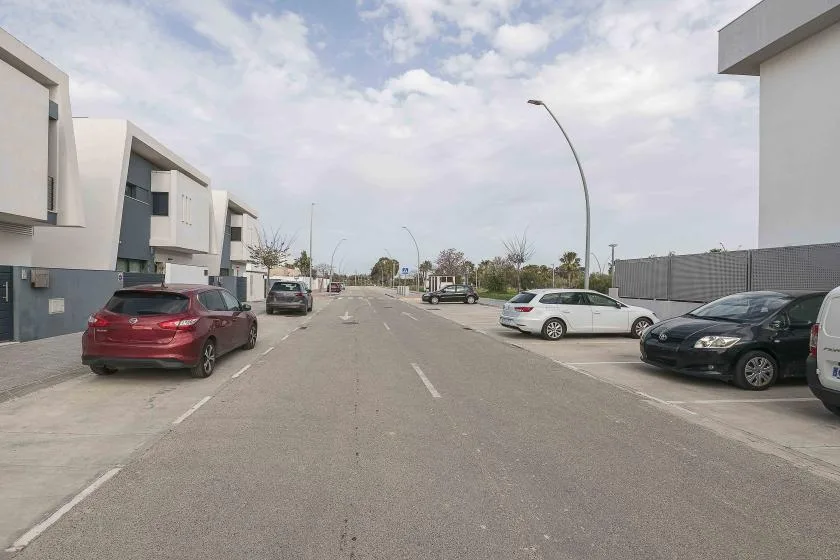 Una calle pavimentada pasa entre edificios modernos, con coches estacionados a ambos lados.