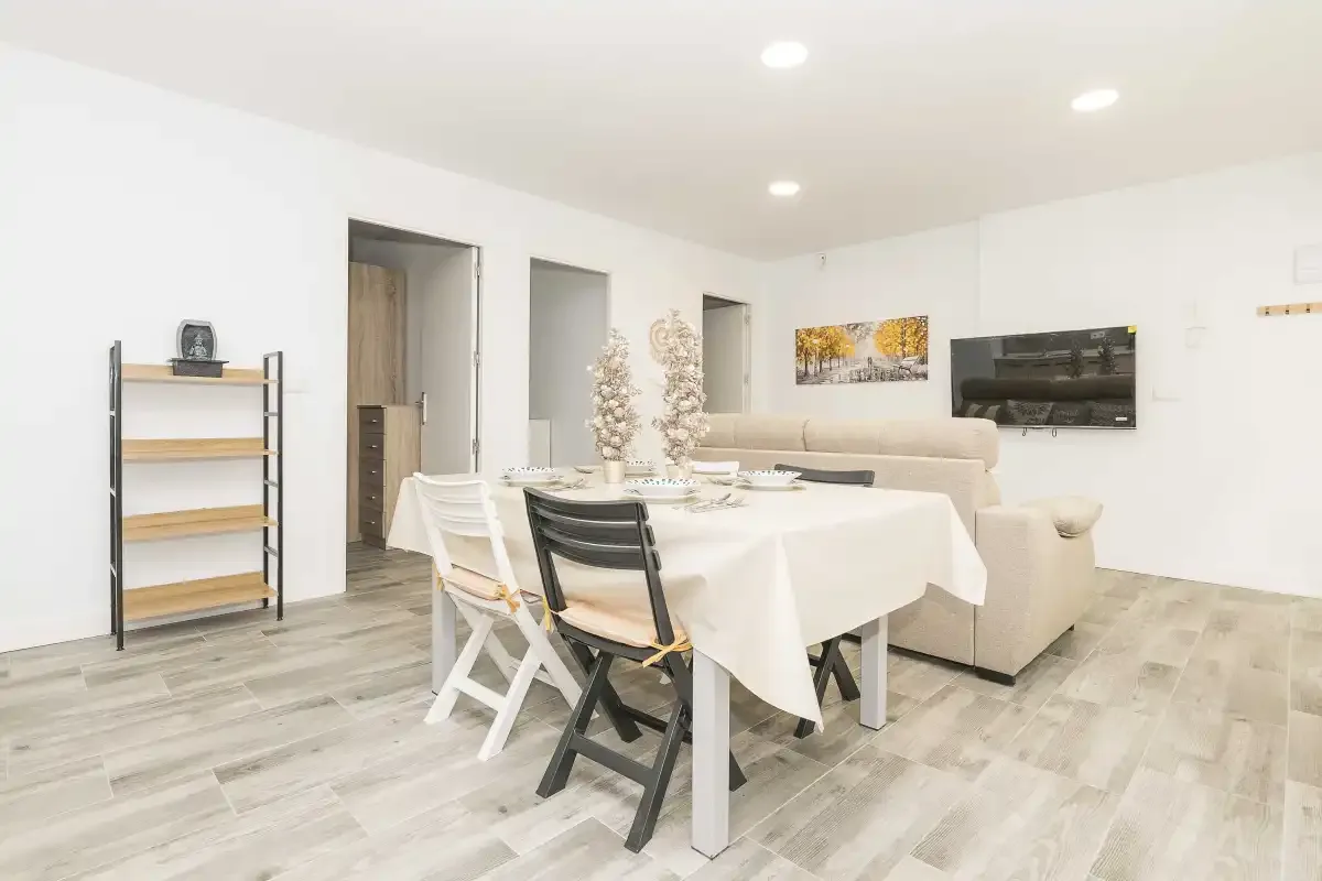 Una luminosa zona de comedor y estar con una mesa, asientos y un televisor en la pared.