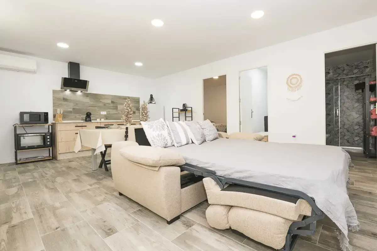 Un dormitorio diáfano con zona de cocina, cama y asientos.