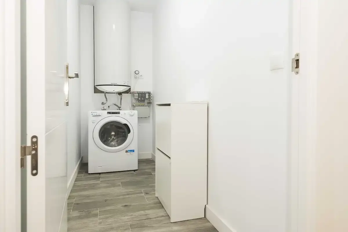 Una zona de lavandería con una lavadora de carga frontal y suelo de baldosas grises.