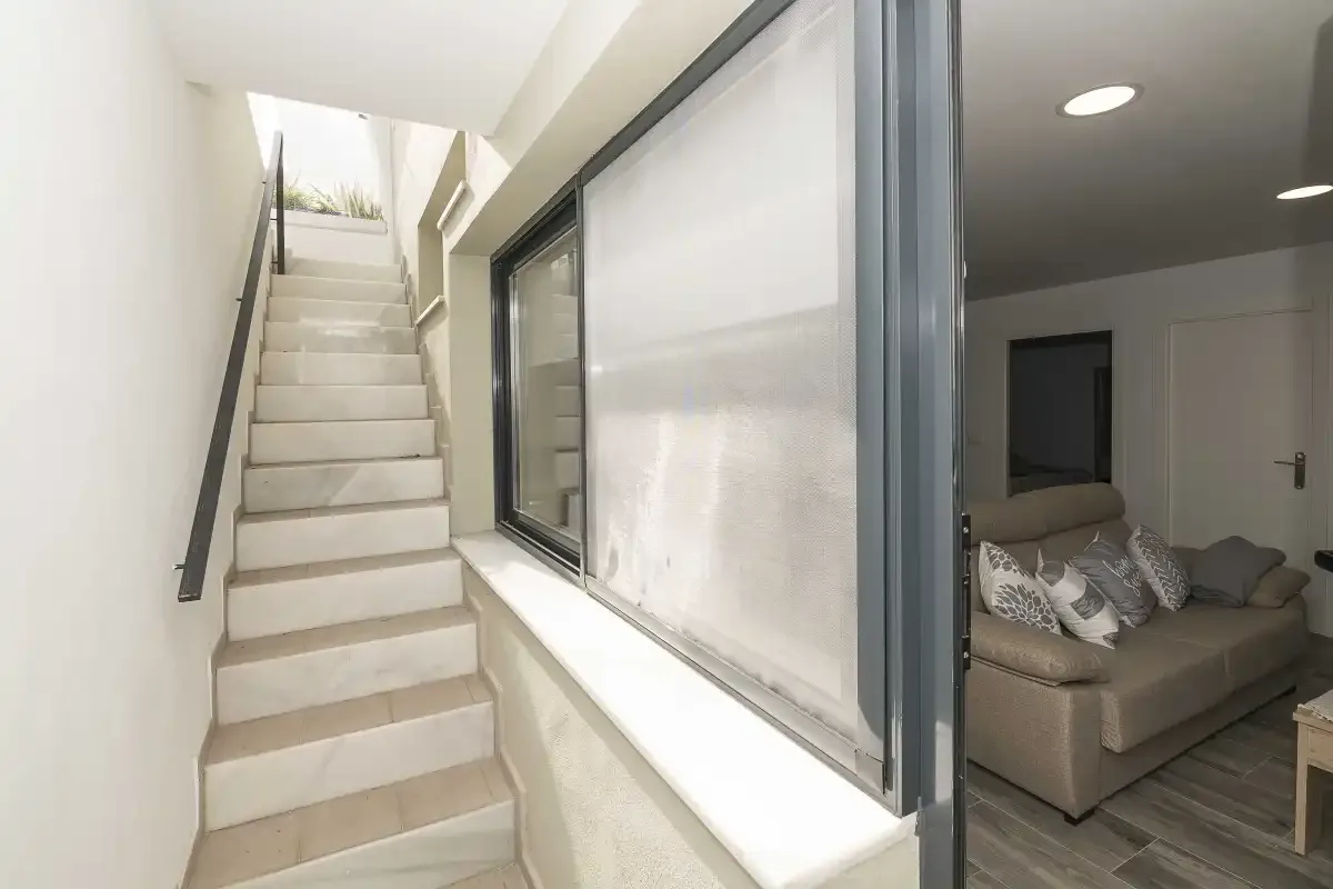 Una escalera junto a una ventana amplia da a una sala de estar con asientos.