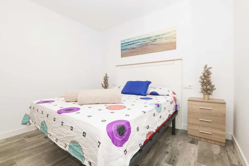 Un dormitorio con una cama cubierta con ropa de cama estampada y una pequeña cómoda junto a ella.