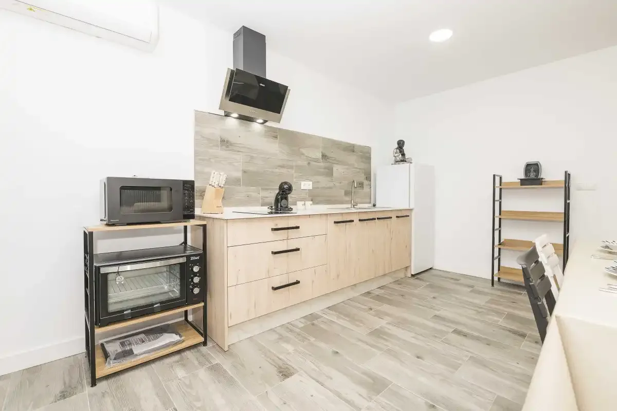 Una cocina luminosa con gabinetes claros, una placa de cocción y electrodomésticos sobre la encimera.