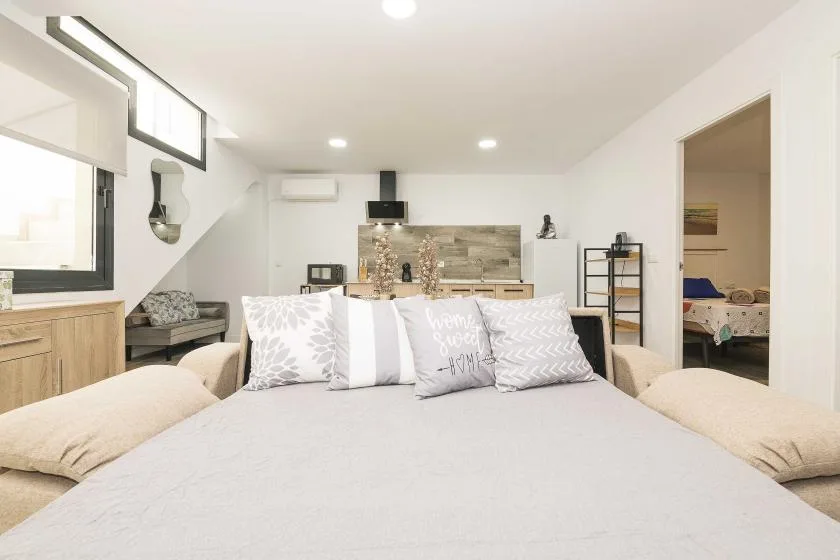Un dormitorio luminoso con una cama grande y una pequeña cocina al fondo.