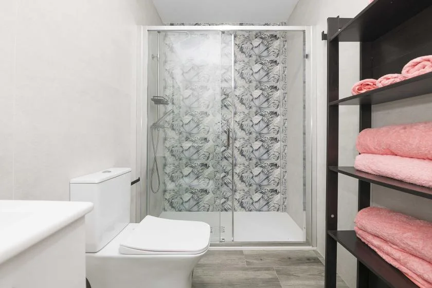 Un baño con inodoro, ducha de vidrio y estantes con toallas dobladas.