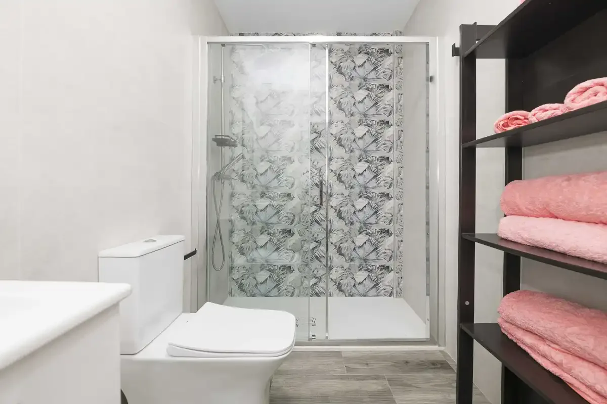 Un baño con una ducha de vidrio y toallas rosas dobladas en estantes abiertos.