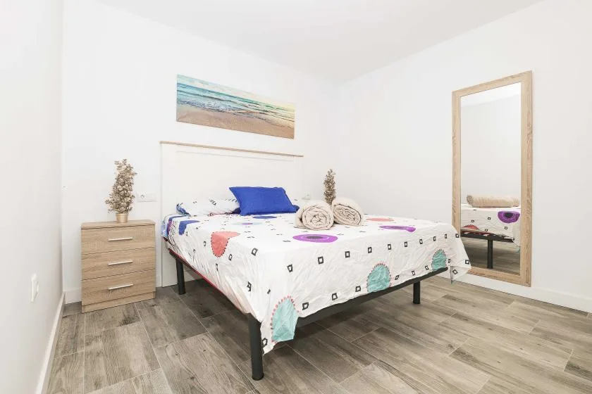 A bright bedroom with a double bed, colorful patterned bedding, and a framed beach picture.