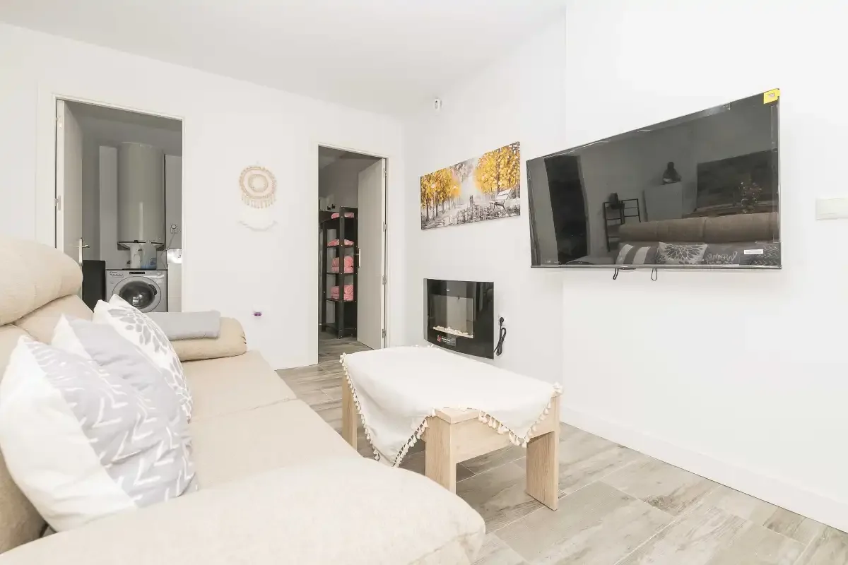 Sala de estar con asientos claros, un televisor y una mesa de centro.