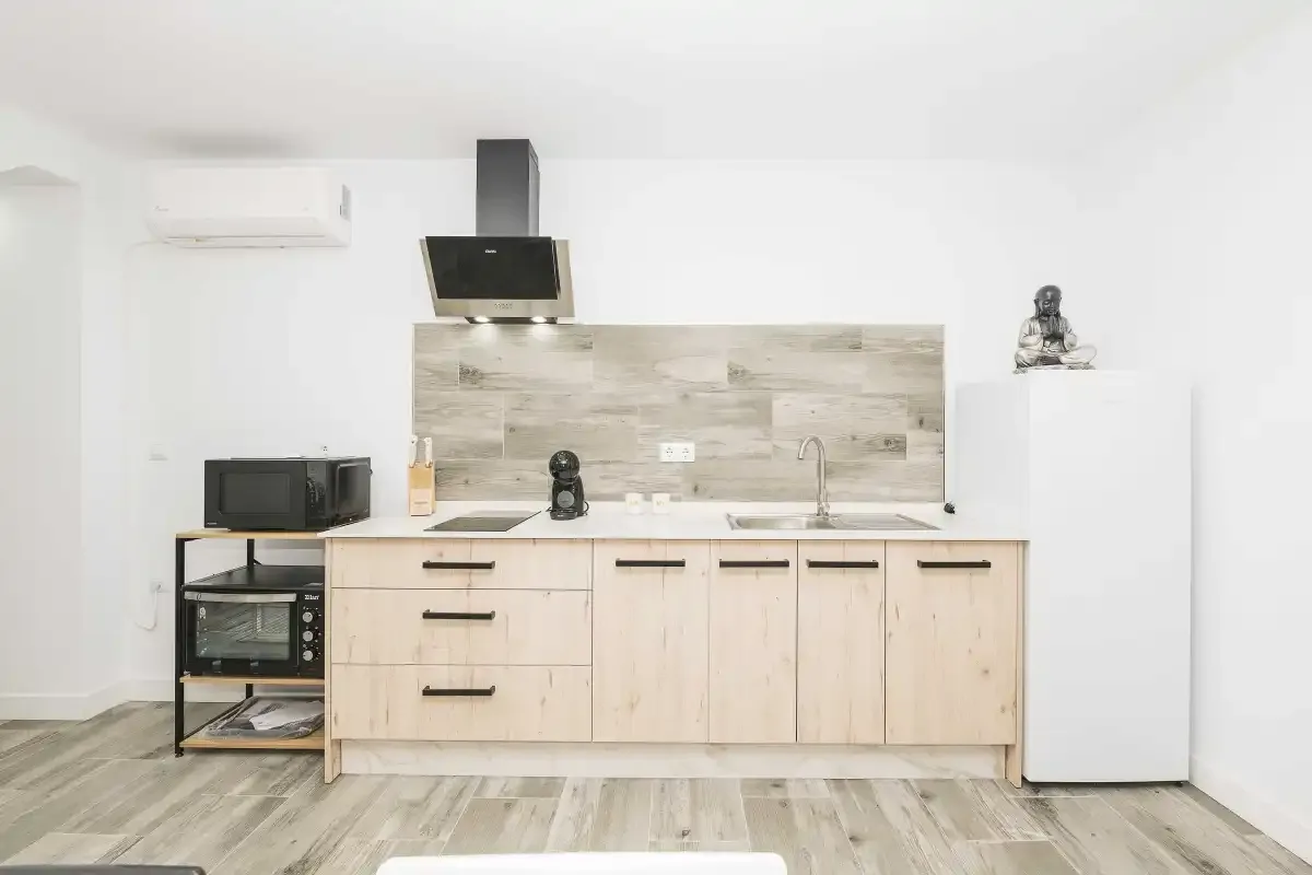 Una cocina luminosa con gabinetes de madera clara, encimera, fregadero y refrigerador.
