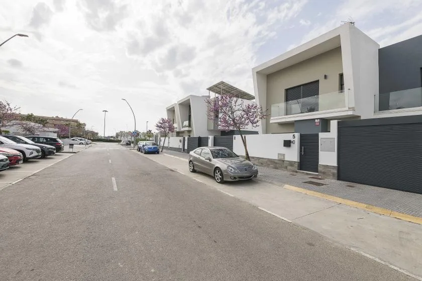 Una calle residencial bordeada de casas blancas modernas y coches aparcados.