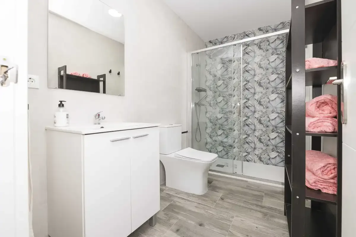 Un baño luminoso con un mueble lavabo blanco y una ducha de cristal.
