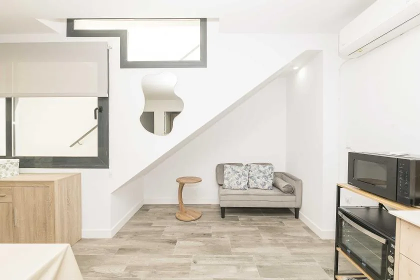 Una luminosa sala de estar con un sofá pequeño bajo una escalera y un televisor cerca.