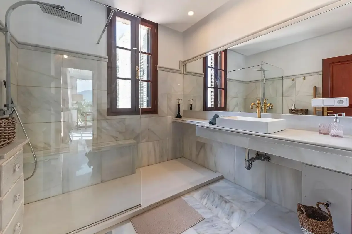 A bright bathroom features a glass shower and a wide sink counter.