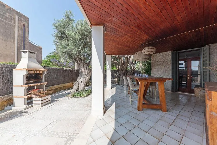 A shaded outdoor dining area with a wooden table beside a paved patio.