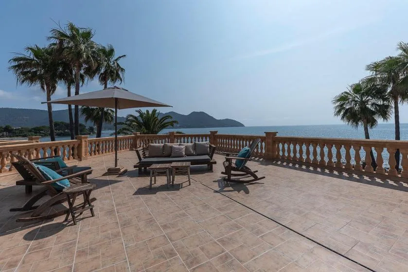A tiled outdoor terrace with seating, palm trees, and a sea view.