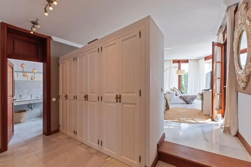A bright bedroom sitting area is visible beyond a large bank of built-in cabinets.