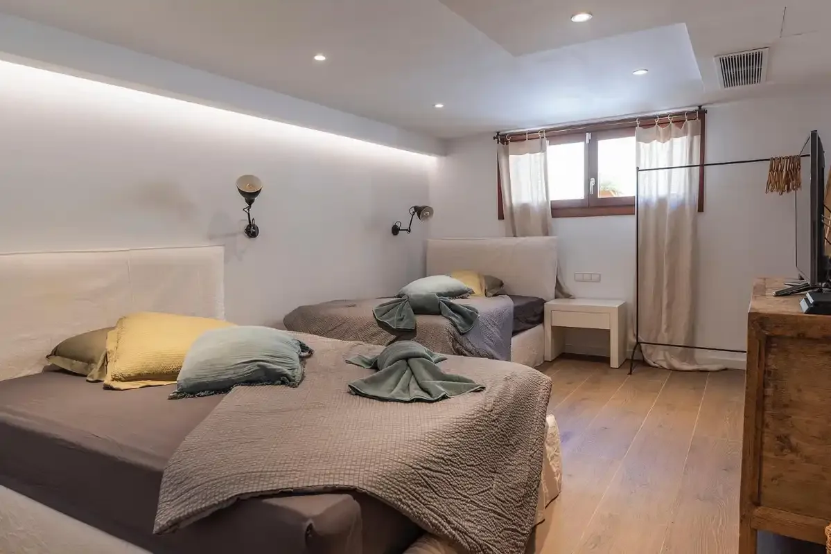 A bedroom with two beds, neutral bedding, and a curtained window.