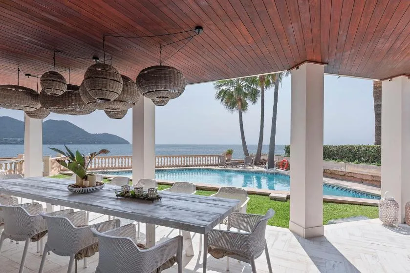 A covered outdoor dining area overlooks a pool and the sea.