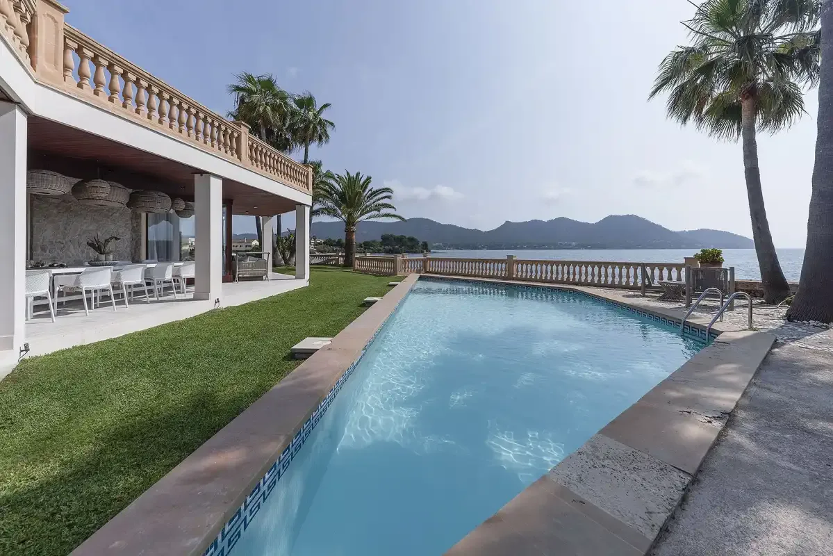 An outdoor swimming pool beside a waterfront terrace and palm trees.