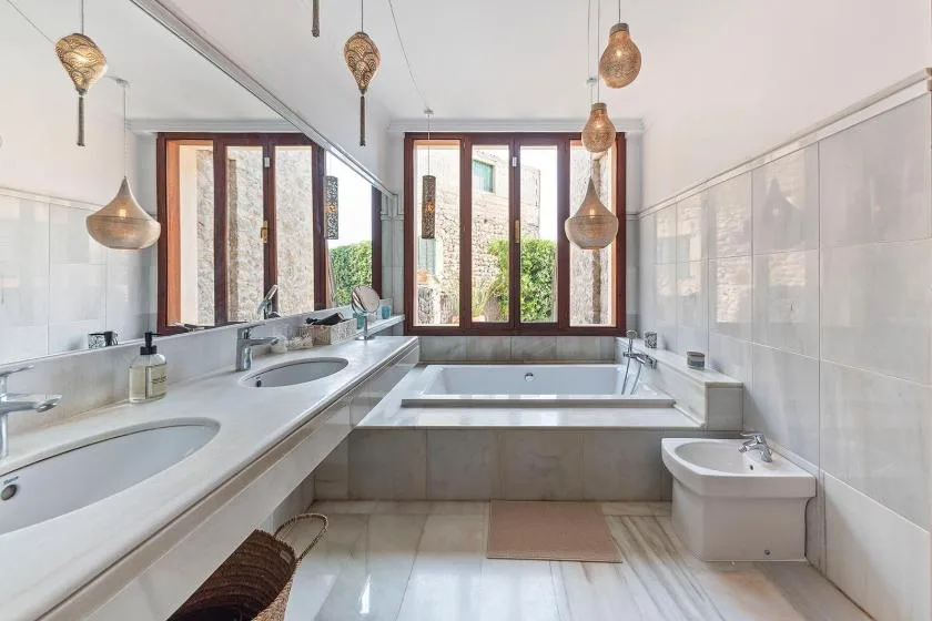 A bathroom with a bathtub, two sinks, and windows overlooking greenery.