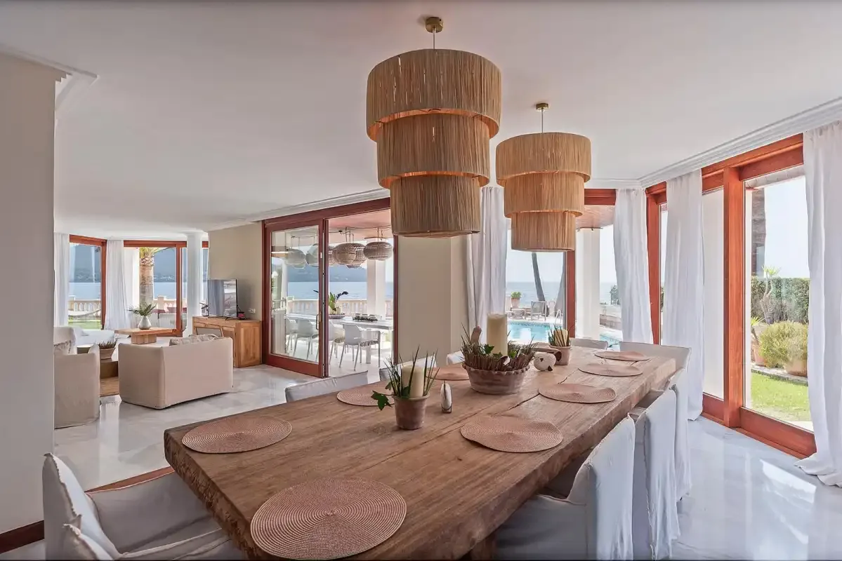 A bright dining area with a long table and views through large windows.