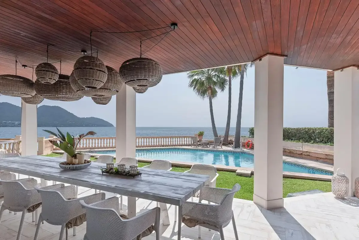A covered outdoor dining area overlooks a swimming pool and the sea.