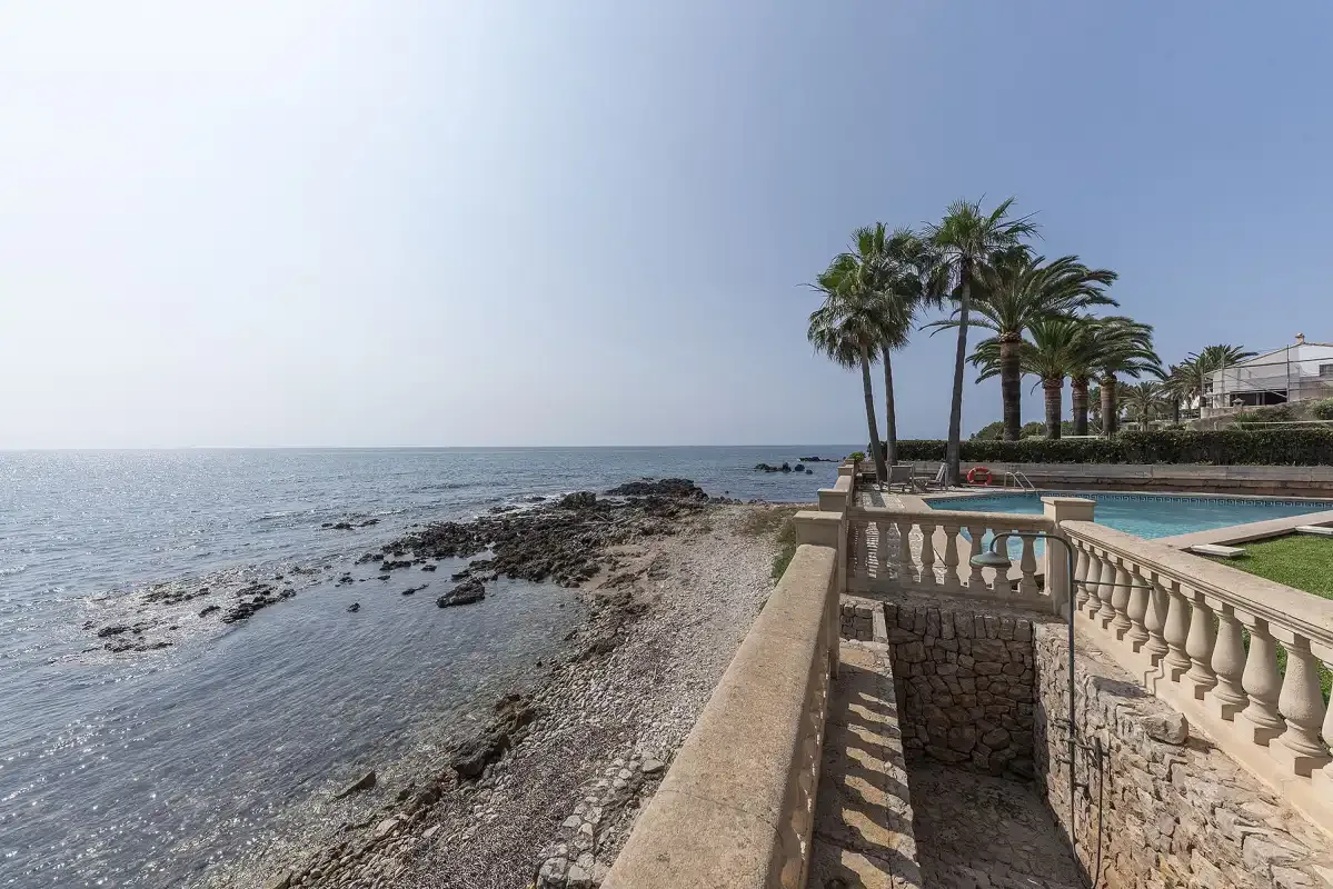 A rocky shoreline beside a seaside terrace and swimming pool.