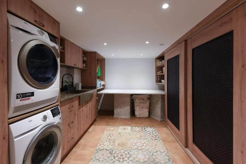 A laundry room with stacked washing machines, wooden cabinetry, and a counter.