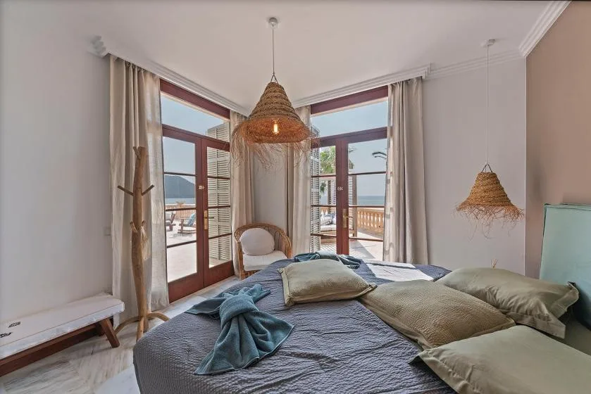 A bedroom with a bed beside large windows overlooking the water.