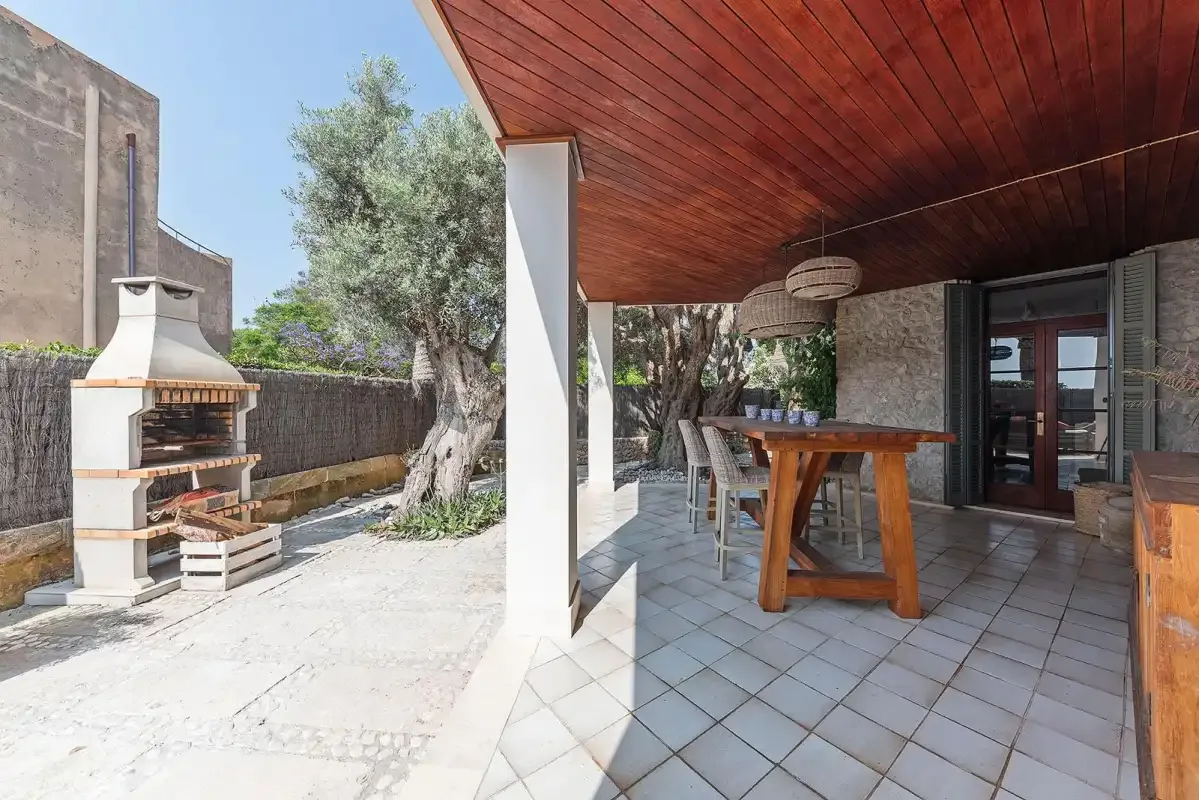 A covered outdoor dining area opens onto a paved patio with a built-in barbecue.