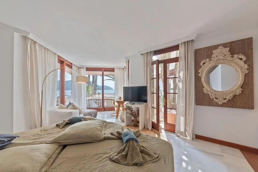 A bright bedroom with a bed, a television, and tall windows.