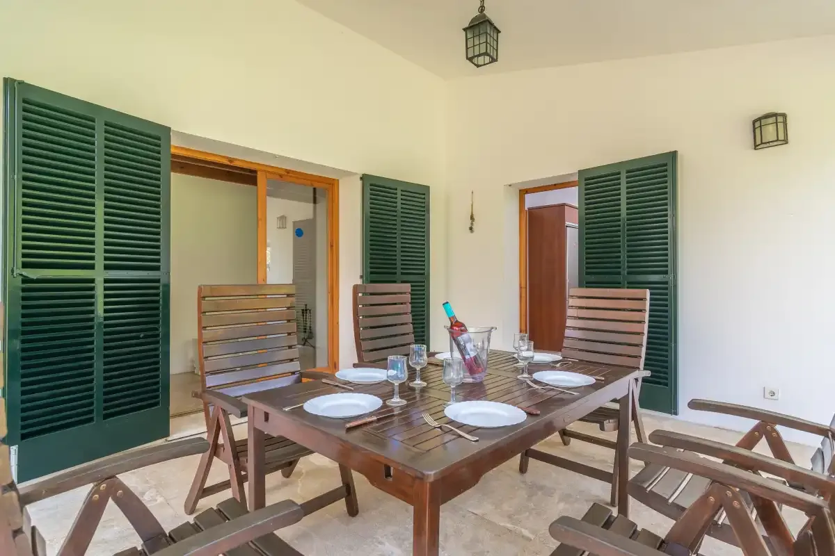 Un comedor con una mesa de madera y sillas junto a contraventanas verdes abiertas.
