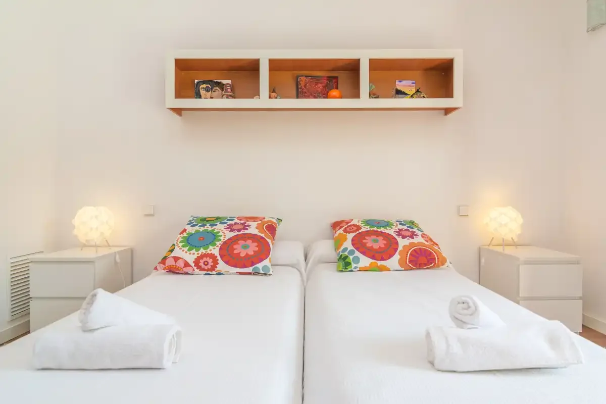 Un dormitorio con dos camas, almohadas coloridas y mesitas de noche a juego.