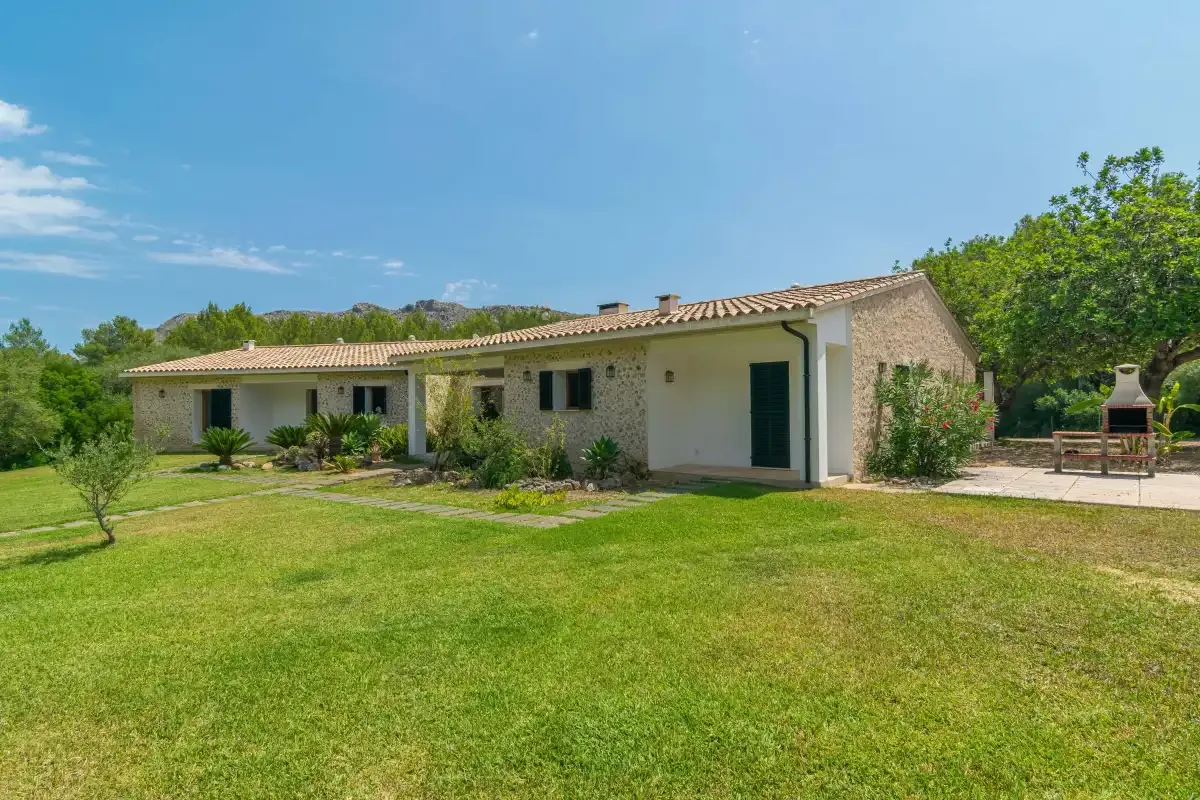 Una casa de una planta se alza junto a un amplio césped verde y un jardín.