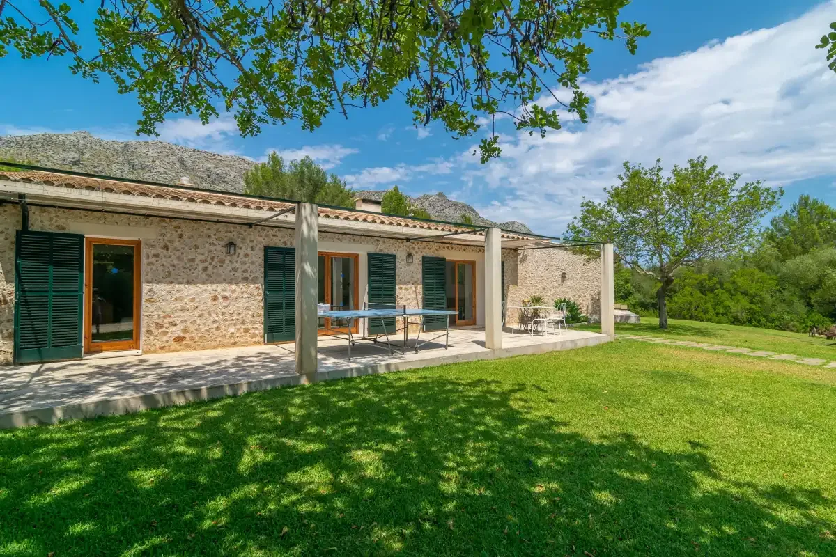 Una casa de piedra da a un patio cubierto junto a un césped verde.