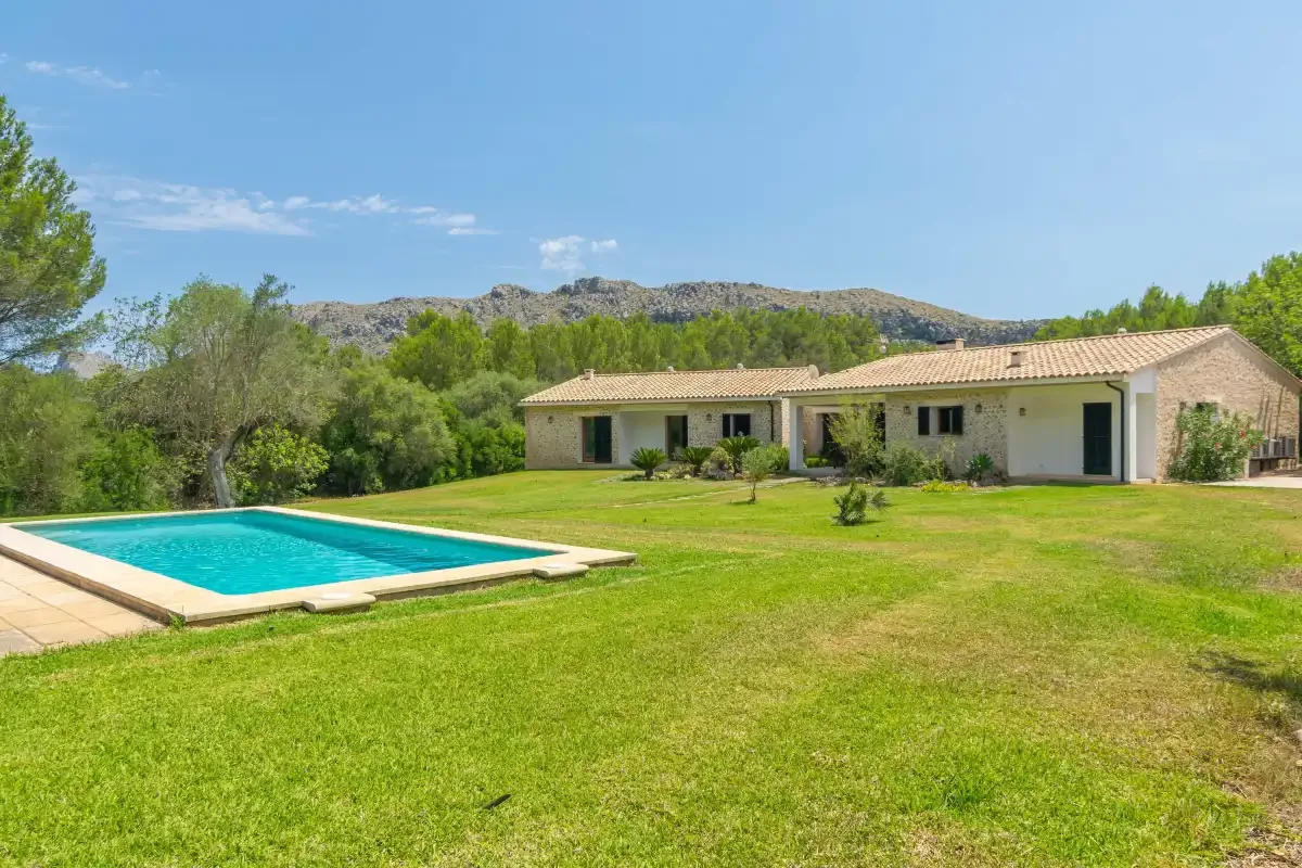 Una casa baja se encuentra junto a una piscina en un amplio césped verde.