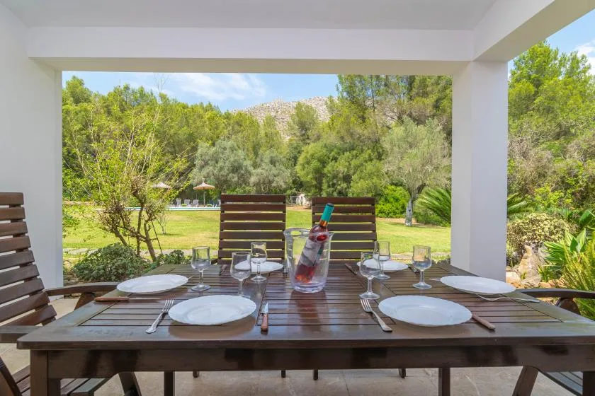 Una mesa de comedor cubierta al aire libre mira hacia un jardín verde y una colina arbolada.