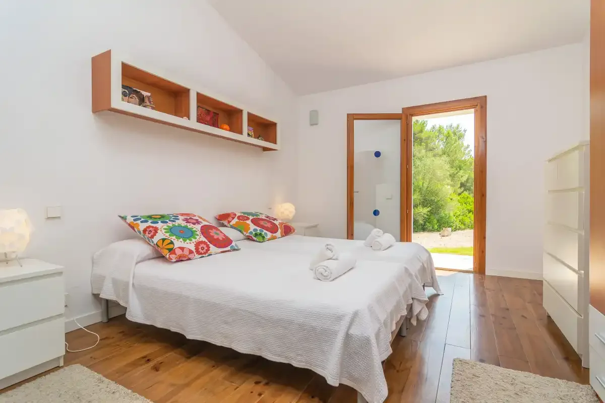 Un dormitorio con una cama tendida, cojines coloridos y una puerta abierta a la vegetación.