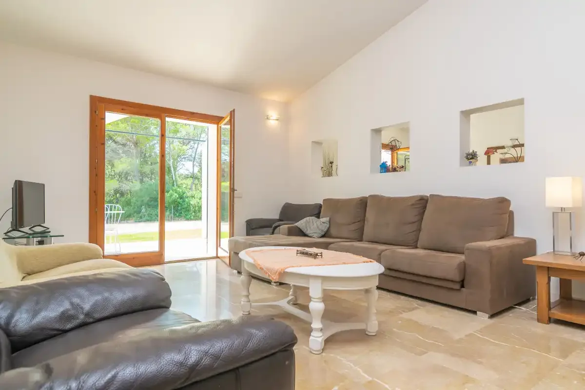 Sala de estar con asientos, una mesa de centro y puertas de vidrio hacia la vegetación.