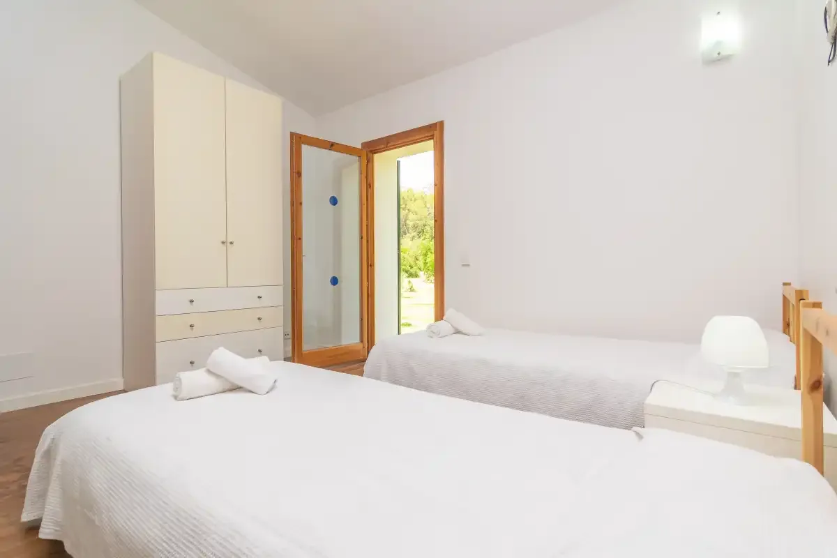 Un dormitorio luminoso con ropa de cama blanca y un armario junto a una puerta abierta.