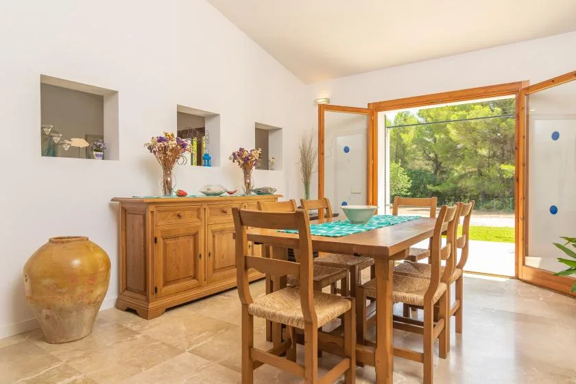Un comedor con una mesa y sillas de madera junto a puertas de vidrio abiertas.