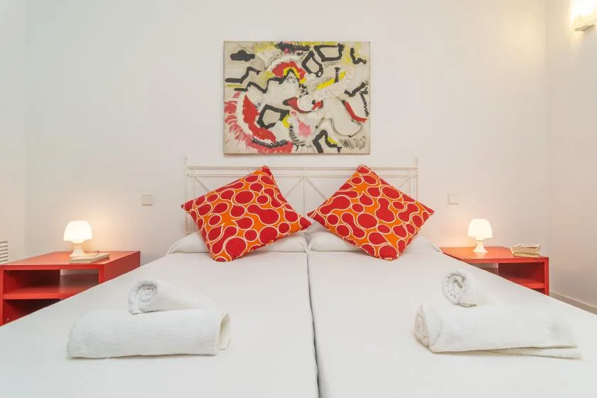 Un dormitorio con dos camas, cojines coloridos y una pintura abstracta sobre el cabecero.