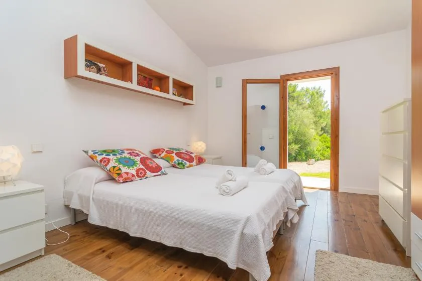 Un dormitorio luminoso con una cama bien hecha y una puerta de vidrio abierta al jardín.